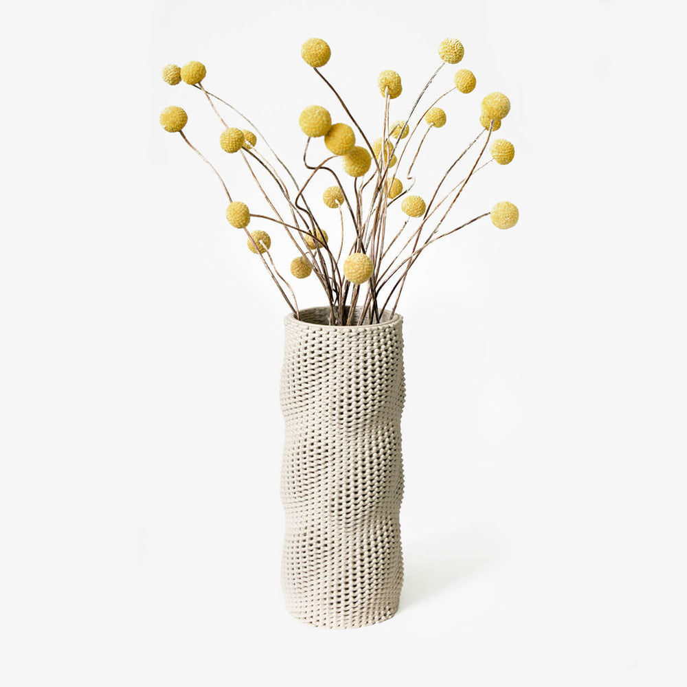 Kilim holding yellow flowers. A 3D printed ceramic vase by Drag And Drop on a white background
