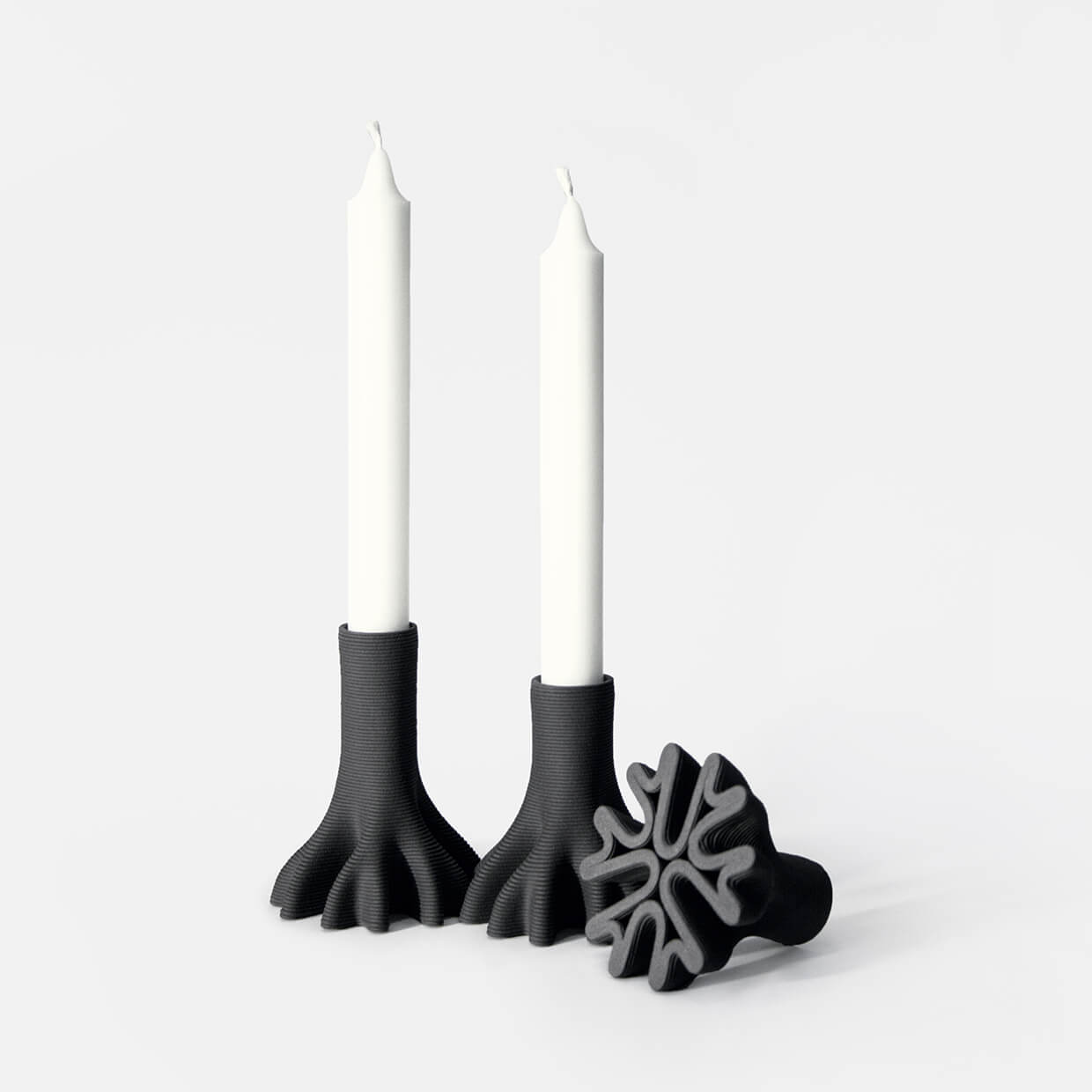 Set of 3 3D Printed Ceramic Candleholders holding candles. One of them is upside down to show the base